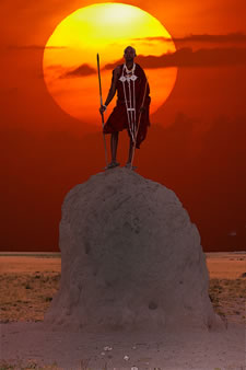 Maasai warrior standing atop termite mound at sunset